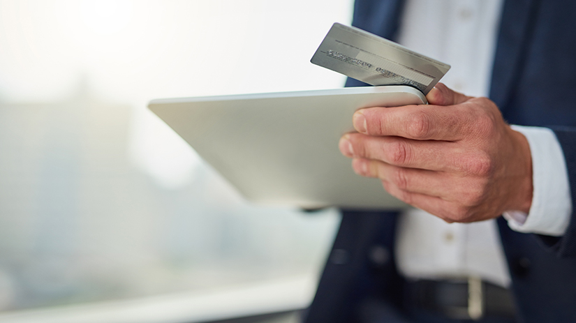 Mężczyzna trzyma kartę płatniczą oraz tablet 